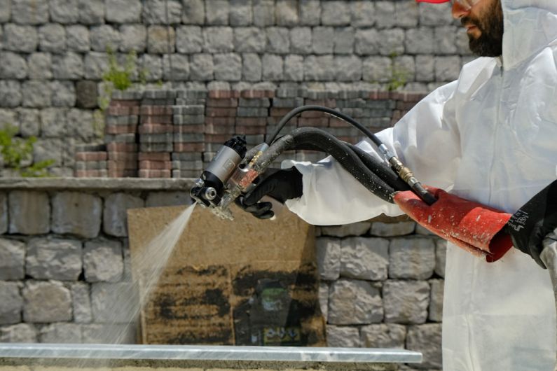 Green Insulation - a man in a white coverall spraying water on a brick wall